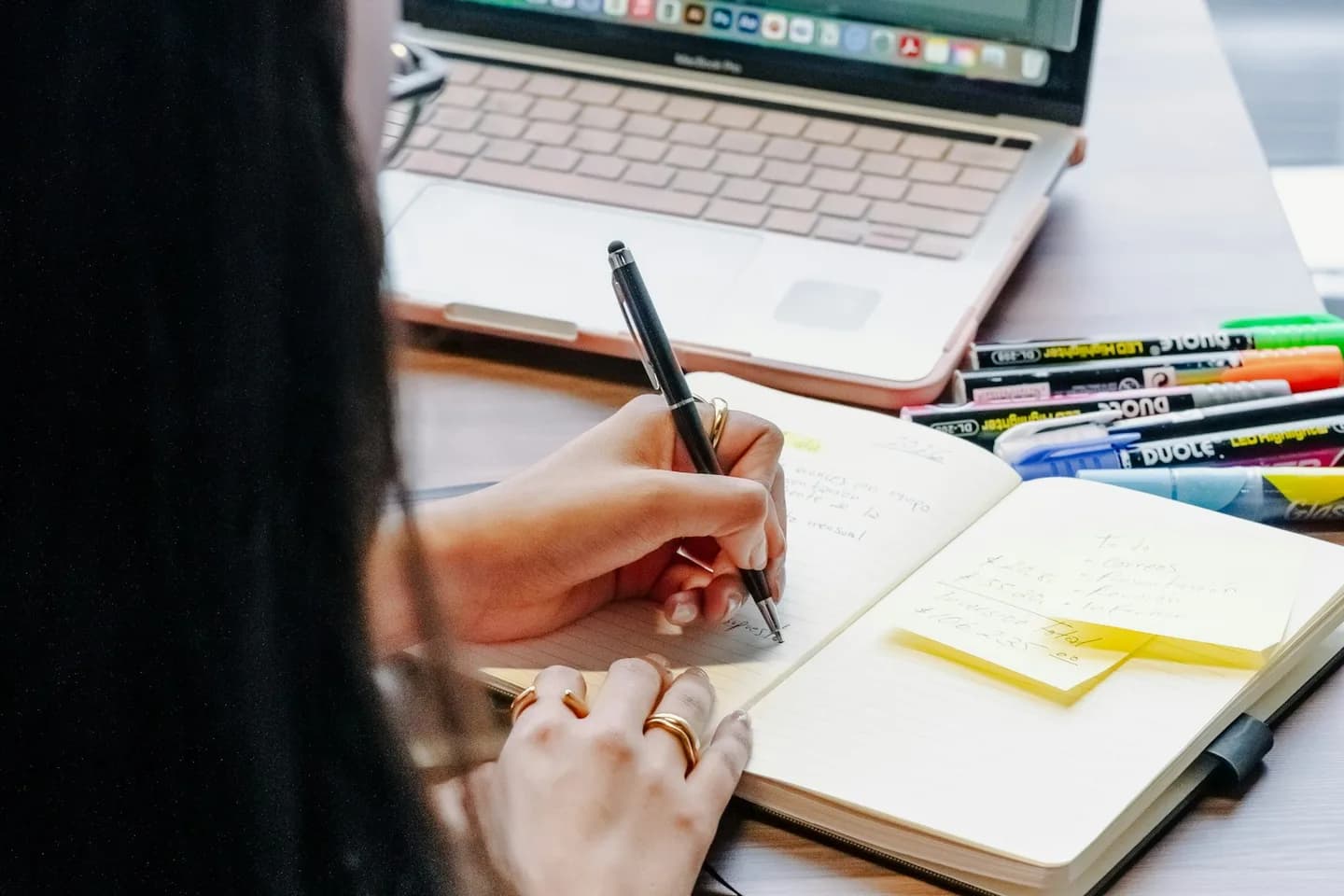 Person taking handwritten notes beside a laptop while reviewing a website layout